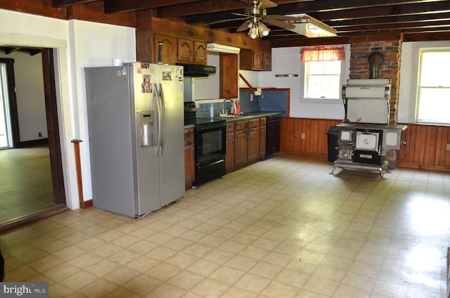 kitchen featuring a wood stove, beamed ceiling, black appliances, and a healthy amount of sunlight