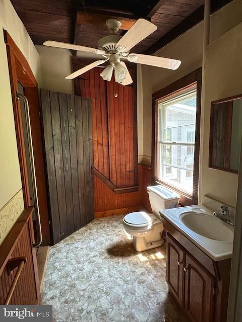 bathroom featuring wooden walls, wood ceiling, toilet, vanity, and ceiling fan