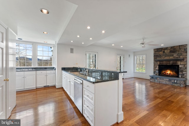 kitchen with white cabinets, a stone fireplace, stainless steel dishwasher, and light hardwood / wood-style flooring