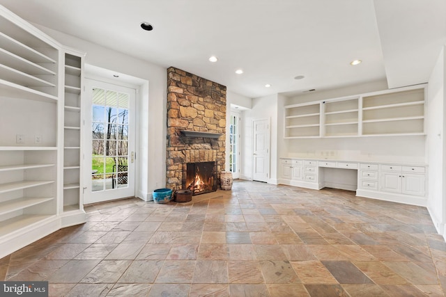 unfurnished living room with built in features, built in desk, light tile flooring, and a stone fireplace