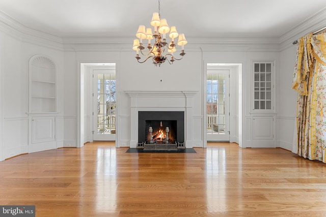 unfurnished living room with a chandelier, plenty of natural light, light hardwood / wood-style floors, and crown molding