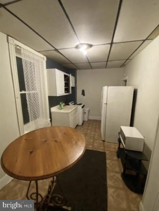 dining space featuring washing machine and clothes dryer, a drop ceiling, and light tile floors