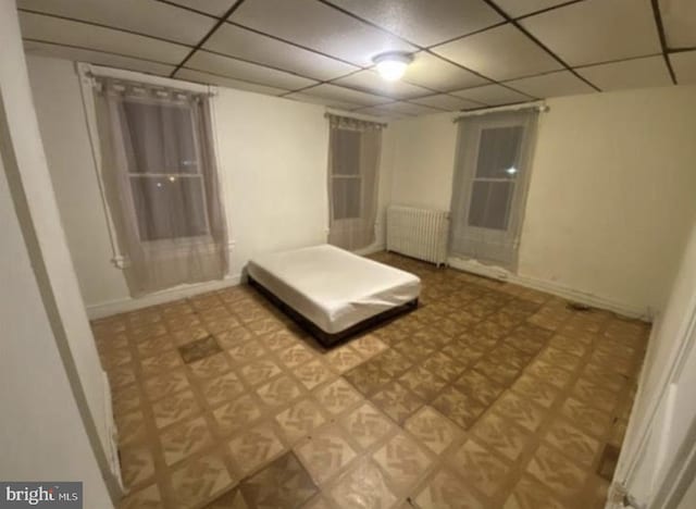 unfurnished bedroom featuring radiator heating unit and a drop ceiling