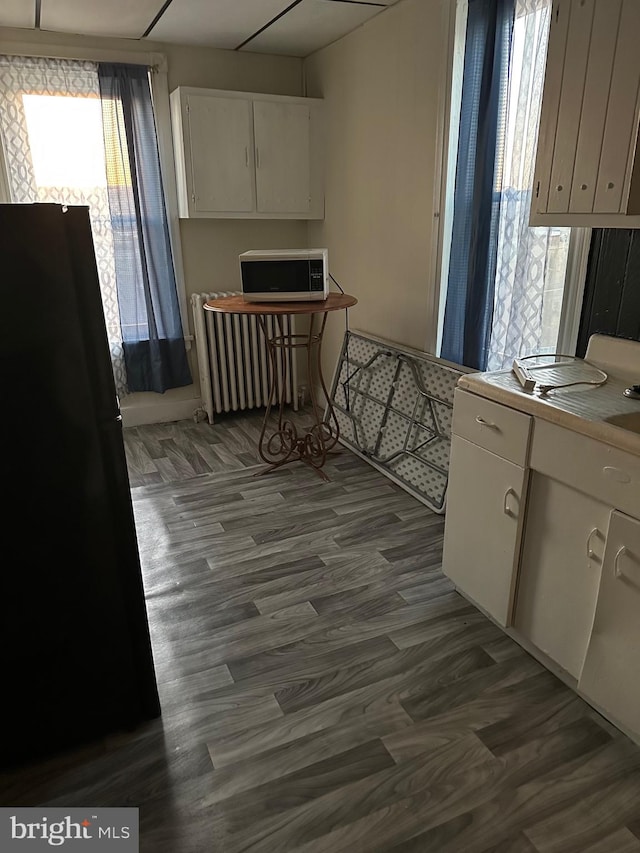 kitchen featuring radiator heating unit, black fridge, dark wood-type flooring, and white cabinetry