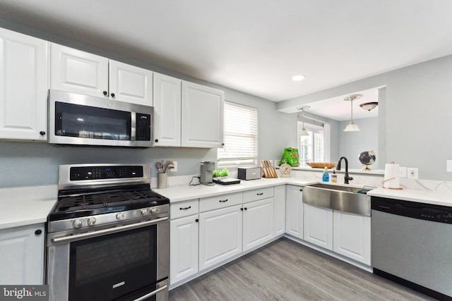 kitchen featuring white cabinets, sink, decorative light fixtures, light hardwood / wood-style floors, and stainless steel appliances