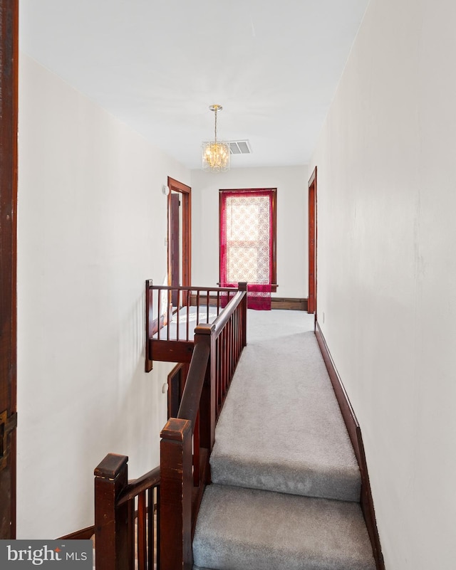 stairs featuring an inviting chandelier and light colored carpet