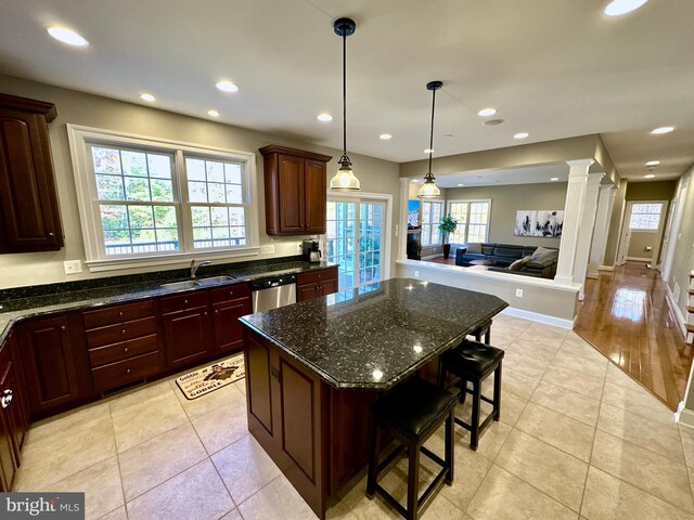 kitchen with decorative columns, light tile patterned flooring, stainless steel dishwasher, open floor plan, and a center island