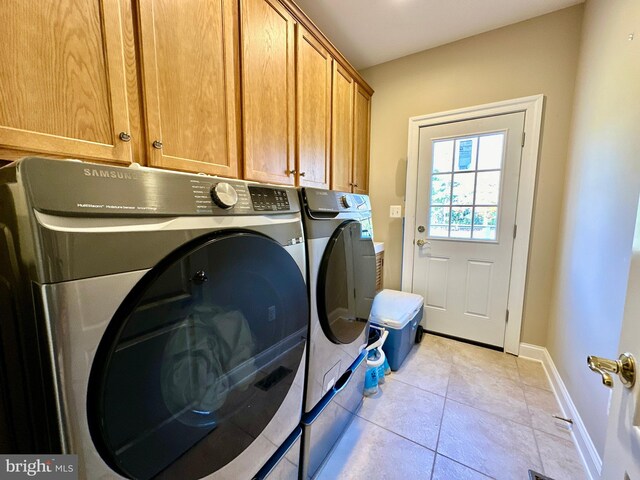 clothes washing area featuring cabinet space, light tile patterned floors, washer and dryer, and baseboards