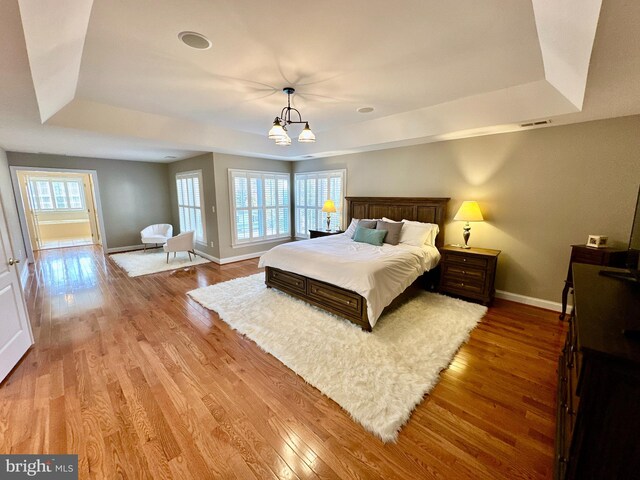 bedroom with visible vents, light wood-style flooring, baseboards, and a tray ceiling