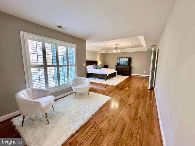 bedroom with visible vents, a raised ceiling, baseboards, and wood finished floors