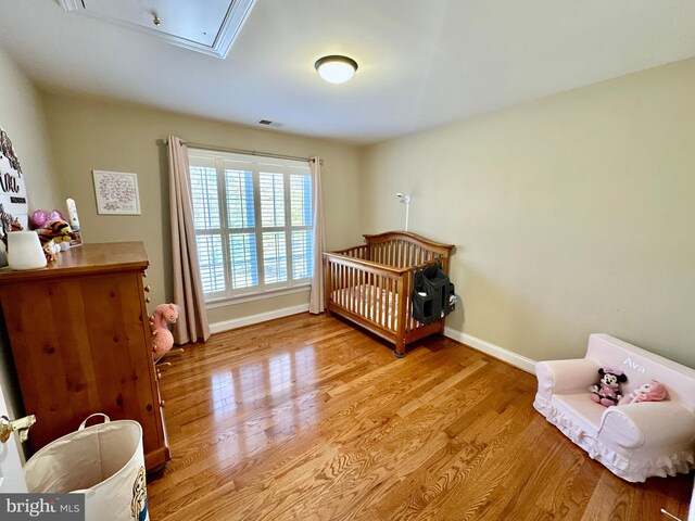 bedroom with light wood-type flooring, baseboards, attic access, and visible vents