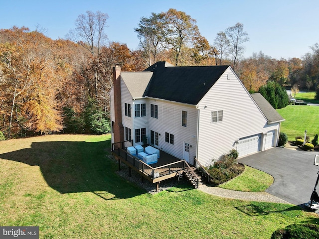 view of property exterior with a deck, aphalt driveway, a yard, a garage, and a chimney