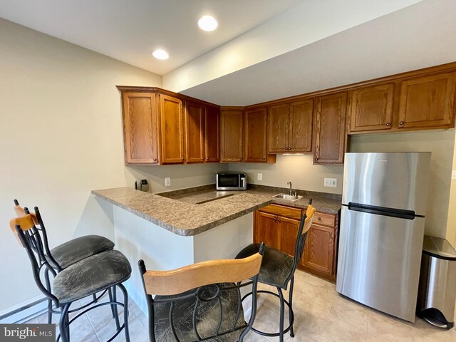 kitchen featuring brown cabinetry, a peninsula, recessed lighting, a sink, and appliances with stainless steel finishes