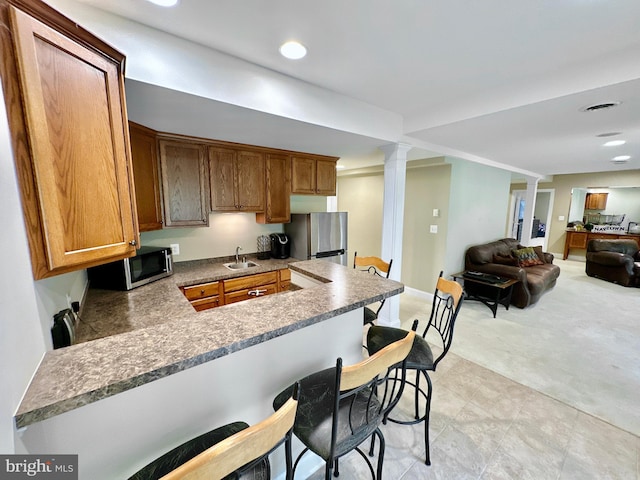 kitchen featuring decorative columns, a peninsula, a kitchen breakfast bar, stainless steel appliances, and a sink