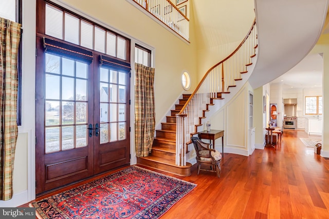 foyer entrance with french doors, wood-type flooring, and a high ceiling