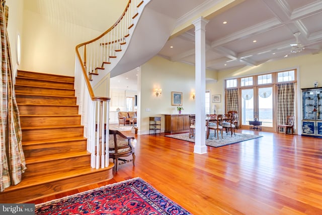 interior space with a towering ceiling, hardwood / wood-style floors, decorative columns, crown molding, and beam ceiling