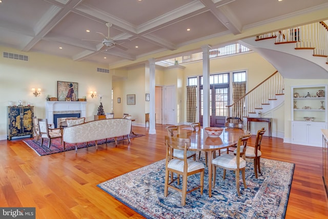 dining space featuring decorative columns, coffered ceiling, light hardwood / wood-style flooring, and beamed ceiling