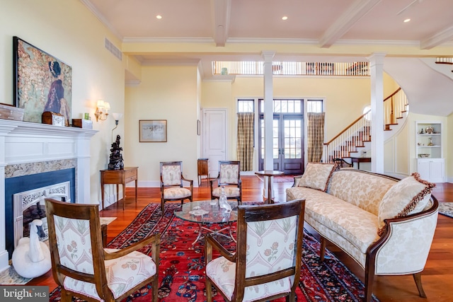 living room featuring a high end fireplace, beamed ceiling, wood-type flooring, and ornate columns