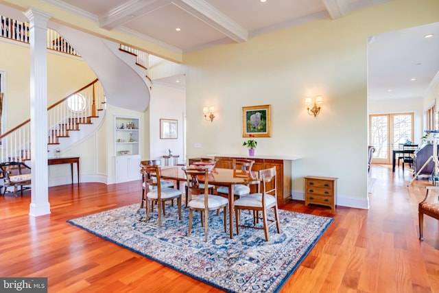 dining space featuring ornate columns, built in features, beam ceiling, crown molding, and light wood-type flooring