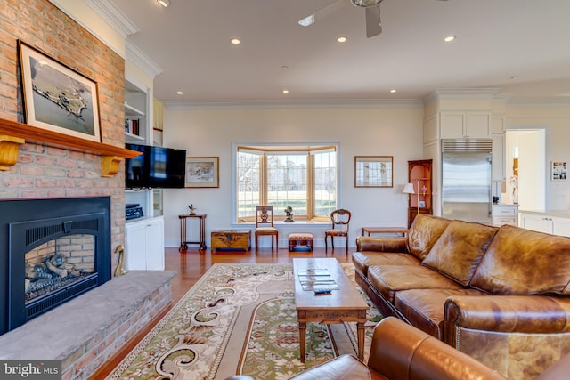 living room featuring built in shelves, crown molding, wood-type flooring, ceiling fan, and a fireplace