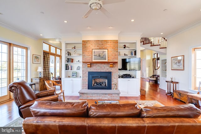 living room with crown molding, a brick fireplace, light wood-type flooring, built in features, and ceiling fan