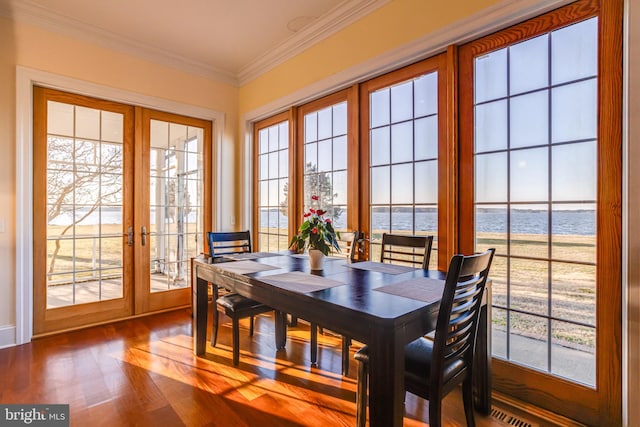 dining area with a water view, a healthy amount of sunlight, crown molding, and french doors