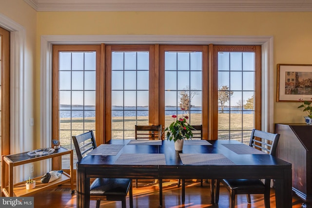 dining space featuring wood-type flooring, ornamental molding, and a water view