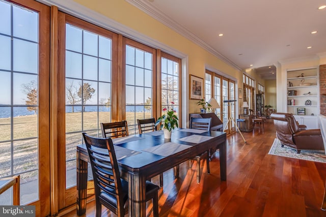 dining room with wood-type flooring, a water view, ornamental molding, and built in features