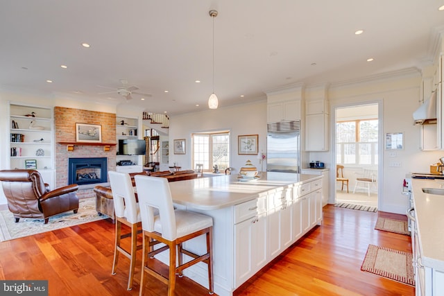 kitchen featuring white cabinetry, hanging light fixtures, light hardwood / wood-style flooring, stainless steel built in fridge, and an island with sink