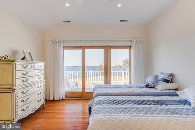 bedroom with access to exterior, vaulted ceiling, light hardwood / wood-style floors, and a water view