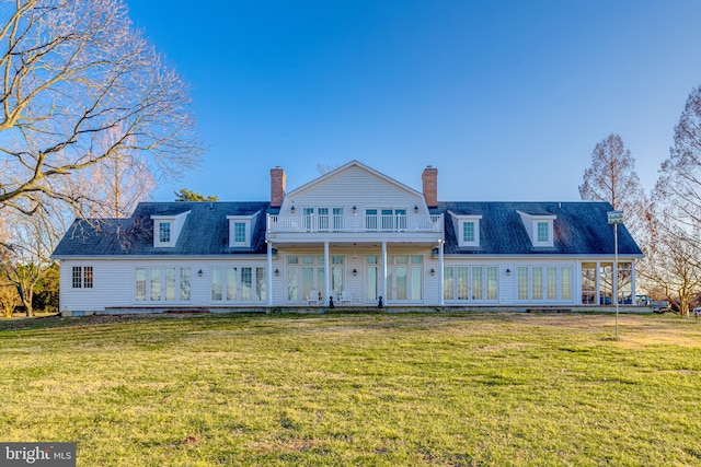 rear view of house with a balcony, a yard, and french doors