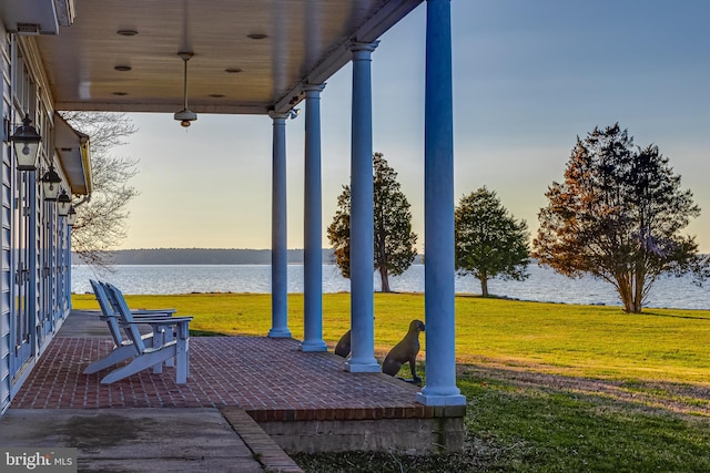 patio terrace at dusk featuring a water view and a lawn