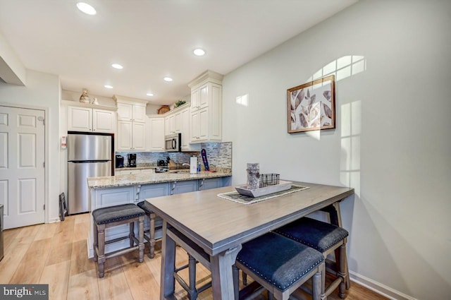 kitchen with light hardwood / wood-style floors, kitchen peninsula, stainless steel appliances, backsplash, and light stone countertops