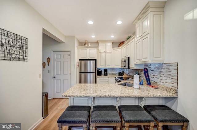 kitchen with appliances with stainless steel finishes, tasteful backsplash, light hardwood / wood-style floors, and kitchen peninsula