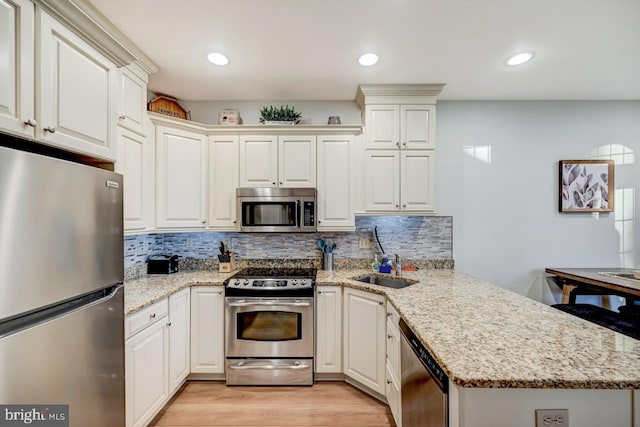 kitchen featuring backsplash, kitchen peninsula, light wood-type flooring, and appliances with stainless steel finishes