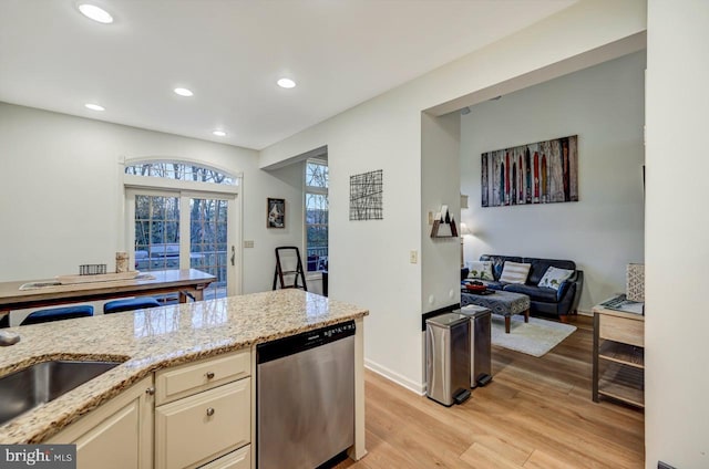 kitchen with light stone countertops, stainless steel dishwasher, light wood-type flooring, sink, and cream cabinetry