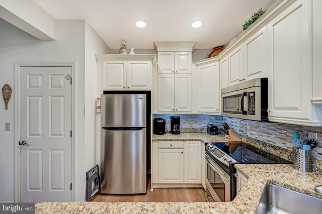 kitchen featuring light hardwood / wood-style floors, tasteful backsplash, stainless steel appliances, light stone counters, and white cabinetry