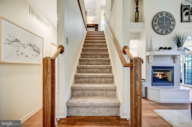 stairs with a towering ceiling, a fireplace, and wood-type flooring