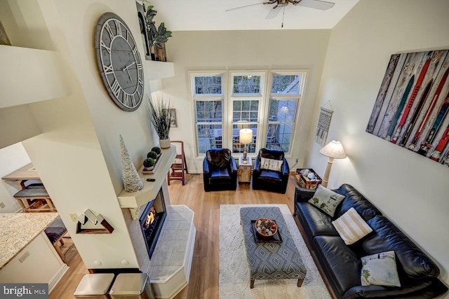 living room with a high ceiling, ceiling fan, a fireplace, and light wood-type flooring