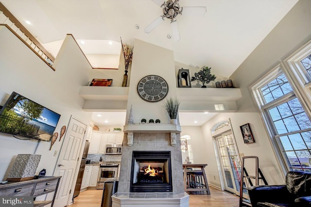 living room featuring a towering ceiling, ceiling fan, light wood-type flooring, and a tile fireplace