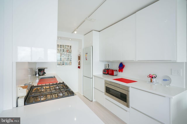 kitchen featuring white fridge, white cabinetry, sink, oven, and track lighting