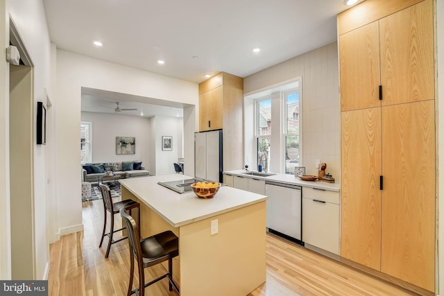 kitchen featuring light hardwood / wood-style floors, a kitchen island, ceiling fan, a breakfast bar area, and dishwasher