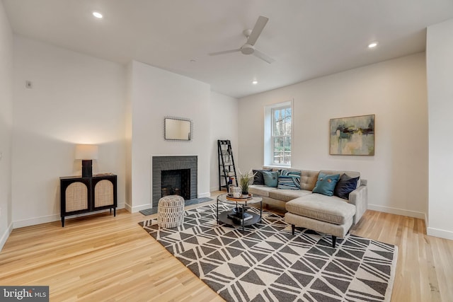 living room featuring light hardwood / wood-style floors, ceiling fan, and a brick fireplace