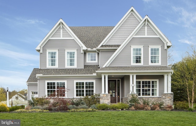 view of front facade with a shingled roof, stone siding, and a front lawn