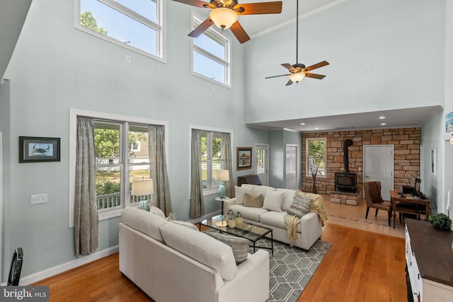 living room with a towering ceiling, a wood stove, ceiling fan, crown molding, and wood-type flooring