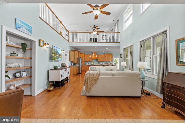 living room with a high ceiling, ceiling fan, and light hardwood / wood-style flooring