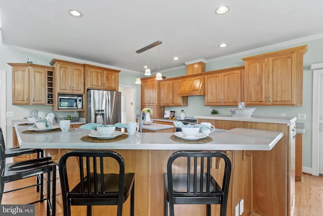 kitchen with light hardwood / wood-style flooring, an island with sink, stainless steel appliances, pendant lighting, and a kitchen bar