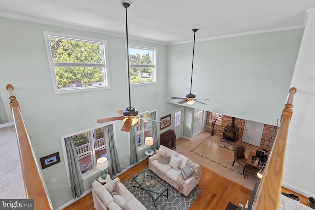 living room featuring ceiling fan, a wood stove, ornamental molding, and hardwood / wood-style flooring