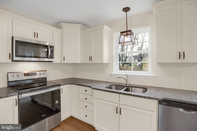 kitchen featuring sink, appliances with stainless steel finishes, hardwood / wood-style flooring, white cabinetry, and pendant lighting