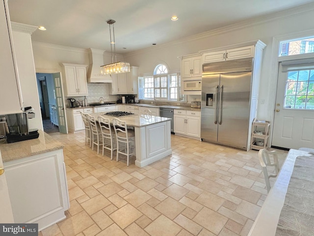 kitchen with a center island, sink, built in appliances, decorative light fixtures, and a kitchen breakfast bar